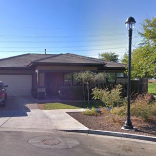 A suburban house with a driveway and a car parked, surrounded by landscaping and a lamp post.