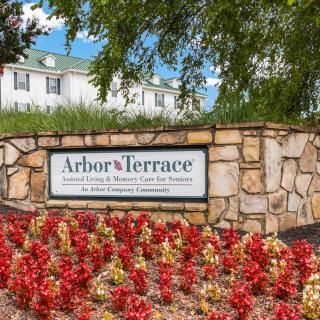 Entrance to Arbor Terrace with a stone sign and vibrant flowers.