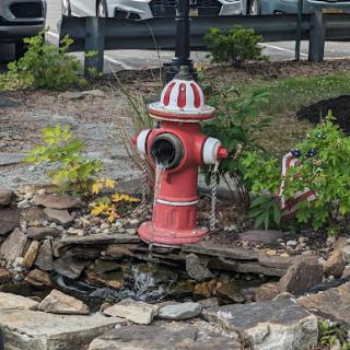 A decorative fire hydrant surrounded by a stone arrangement and greenery, serving as a unique water feature in the landscape.