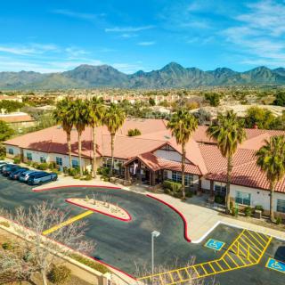 Aerial view of a building surrounded by palm trees with mountains in the background.