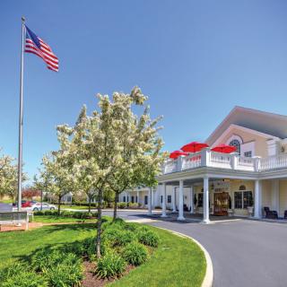 A sunny day at the entrance of a large building with a flag and well-maintained landscaping.