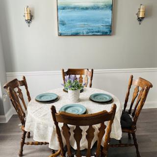 A cozy dining setup featuring a round table with blue plates and a floral centerpiece, complemented by soft wall art.