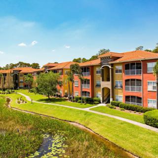 A scenic view of modern apartment buildings surrounded by lush greenery and a serene pond.