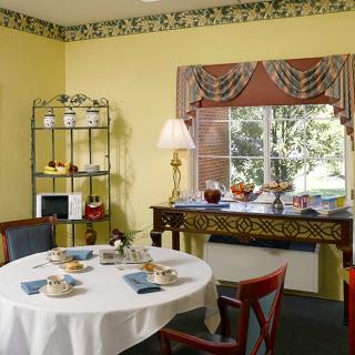 A cozy dining room with a round table set for a meal, featuring warm yellow walls and classic decor.