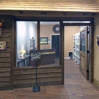 A wooden-themed storefront with an open sign, leading to a cozy interior space and office area.