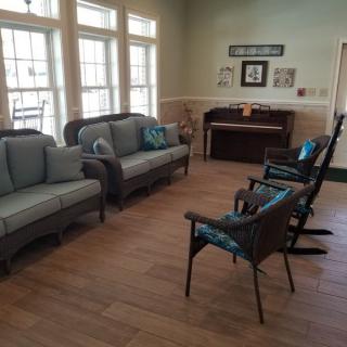 A cozy living room with sofas, rocking chairs, and a piano by large windows.