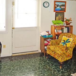 A cozy living room with a vintage yellow chair, bookshelf, and artwork on the walls.