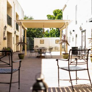 A sunny outdoor patio area with tables, chairs, and a pergola providing some shade.