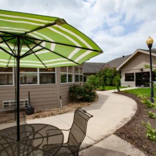 A patio area with a striped green umbrella, outdoor furniture, and a curving pathway leading to a building.