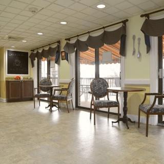 A well-lit waiting area with chairs and tables, featuring large windows and decorative curtains.
