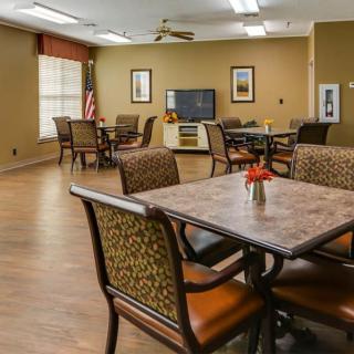 A cozy community room with tables and chairs, featuring a television and decorative elements.