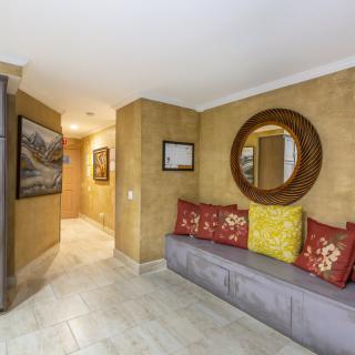 A cozy hallway interior featuring a framed mirror, cushioned seating with colorful pillows, and decorative wall art.