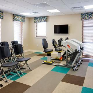 A modern exercise room equipped with fitness machines and chairs, featuring a television on the wall.
