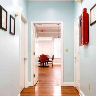 A brightly lit hallway with light blue walls and wooden flooring leading to a room with red chairs.