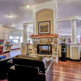 A modern lobby with a cozy seating area in front of a stone fireplace, featuring polished wooden floors and decorative artwork above the mantel.