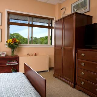 A cozy bedroom with wooden furniture, including a wardrobe and dresser, under natural light from a window.