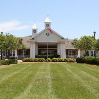 A picturesque view of a building with twin cupolas on a sunny day, framed by a well-manicured lawn and trees.