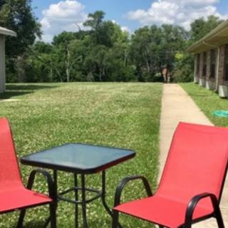 A pair of red chairs and a small glass table on a sunny lawn patio.