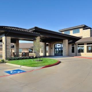 A modern building entrance with a covered driveway and parking area, under a clear blue sky.