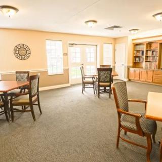 A spacious and well-lit room with tables, chairs, and a bookshelf.