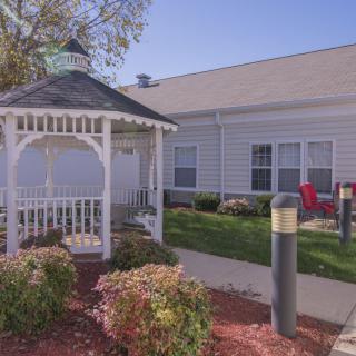 A cozy outdoor gazebo surrounded by garden landscaping next to a building.