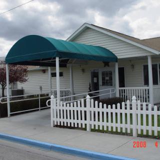 A welcoming building entrance with a green canopy and white picket fence under a cloudy sky.
