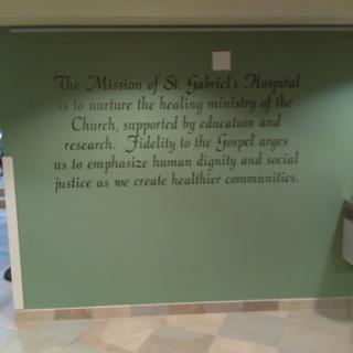 A wall featuring the mission statement of St. Patrick's Hospital, emphasizing the commitment to the healing ministry of the Church and dedication to education and research.