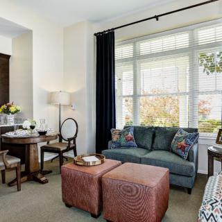 A cozy living and dining area with ample natural light, featuring a sofa, two ottomans, and a small dining table.