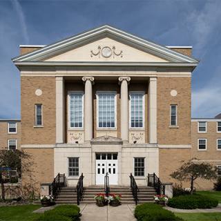 A symmetrical brick building with grand columns at the entrance, likely part of an institutional setting.