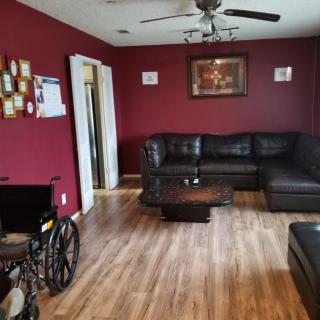 A cozy living room with a dark sectional sofa, wheelchair, and wooden floor.