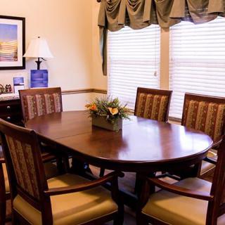 A cozy dining room with a wooden table and chairs, decorated with a central floral arrangement.