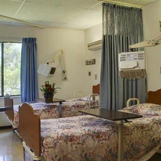 A hospital room with multiple beds, separated by curtains, and a large window.
