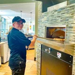 A chef carefully placing a pizza into the oven in a modern restaurant kitchen.