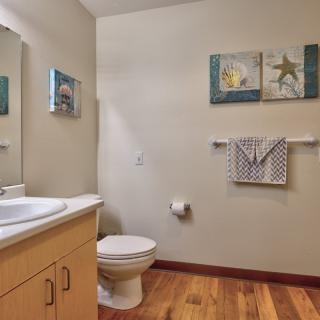 A clean and neatly organized bathroom featuring a sink, toilet, and decorative wall art.