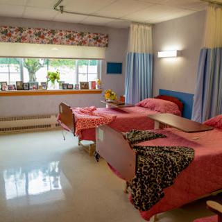 A well-lit hospital room featuring two patient beds with colorful bedding and a view of the outdoors.