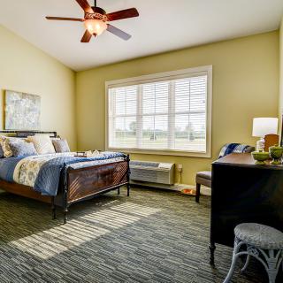 A cozy bedroom with a comfortable bed, a desk, and large window letting in natural light.
