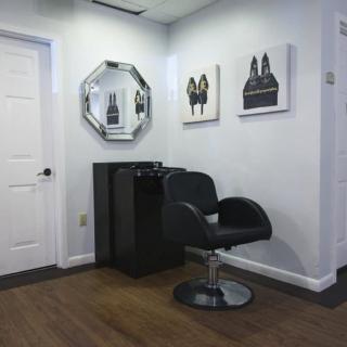 A modern salon interior with a stylist chair, mirror, and artwork on the walls.