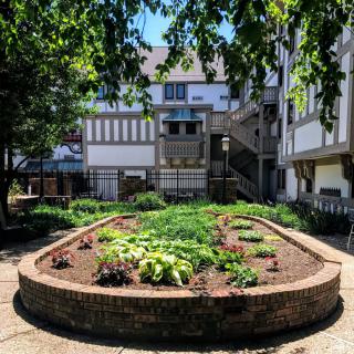 A beautiful garden surrounded by a brick wall, set against a backdrop of Tudor-style architecture.