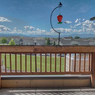 A scenic view from a balcony featuring mountains in the distance and a bird feeder hanging above a wooden railing.