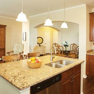 A modern kitchen featuring an island with a granite countertop, sink, and pendant lighting, adjacent to an open dining area.