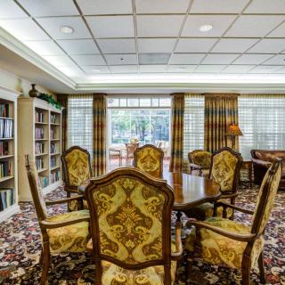 A cozy library room featuring ornate chairs, bookshelves, and large windows with elegant curtains.