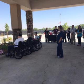 A group of people, including individuals in wheelchairs, participate in an outdoor gathering under a covered area.