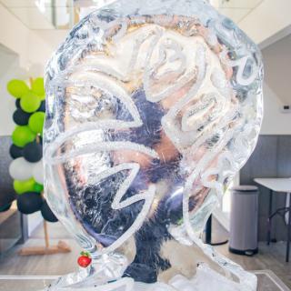 An ice sculpture displayed indoors, surrounded by decorative balloons.