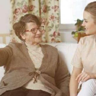 An elderly woman and a young caregiver sitting and chatting in a cozy living room.