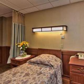 A hospital room with a single bed and a bedside table adorned with flowers.