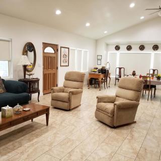 A spacious living room with beige recliners, a dark sofa, and a dining area in the background.