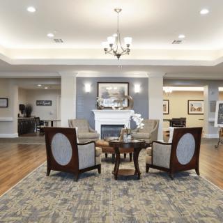 A cozy and elegant living room with a seating area around a fireplace, featuring stylish furniture and a chandelier.