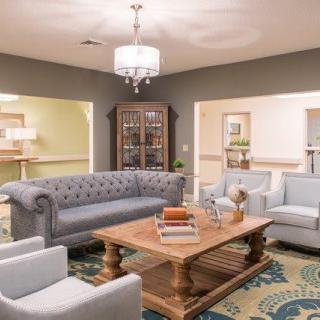 A cozy and elegantly designed living room featuring a plush sofa, armchairs, and a wooden coffee table under a chandelier.