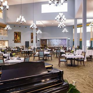 A spacious and elegant dining area with a piano, chandeliers, and well-arranged tables and chairs.