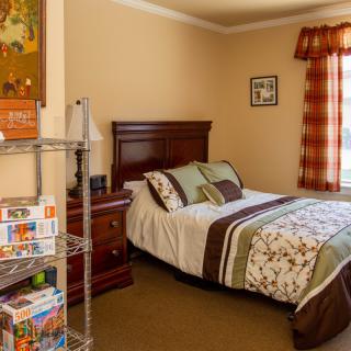 A cozy bedroom with a neatly made bed, nightstand, and shelving unit.